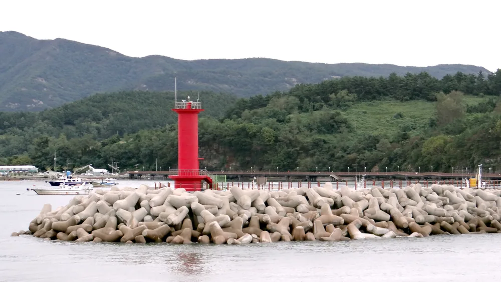 부안 격포항 — 테트라포드를 쌓은 격포항 방파제 끝에 빨간 등대가 서 있고, 뒤로 산과 배들이 보입니다.